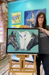 Sarah Perkins in her studio showing her painting of a horse for the Horse Trust charity